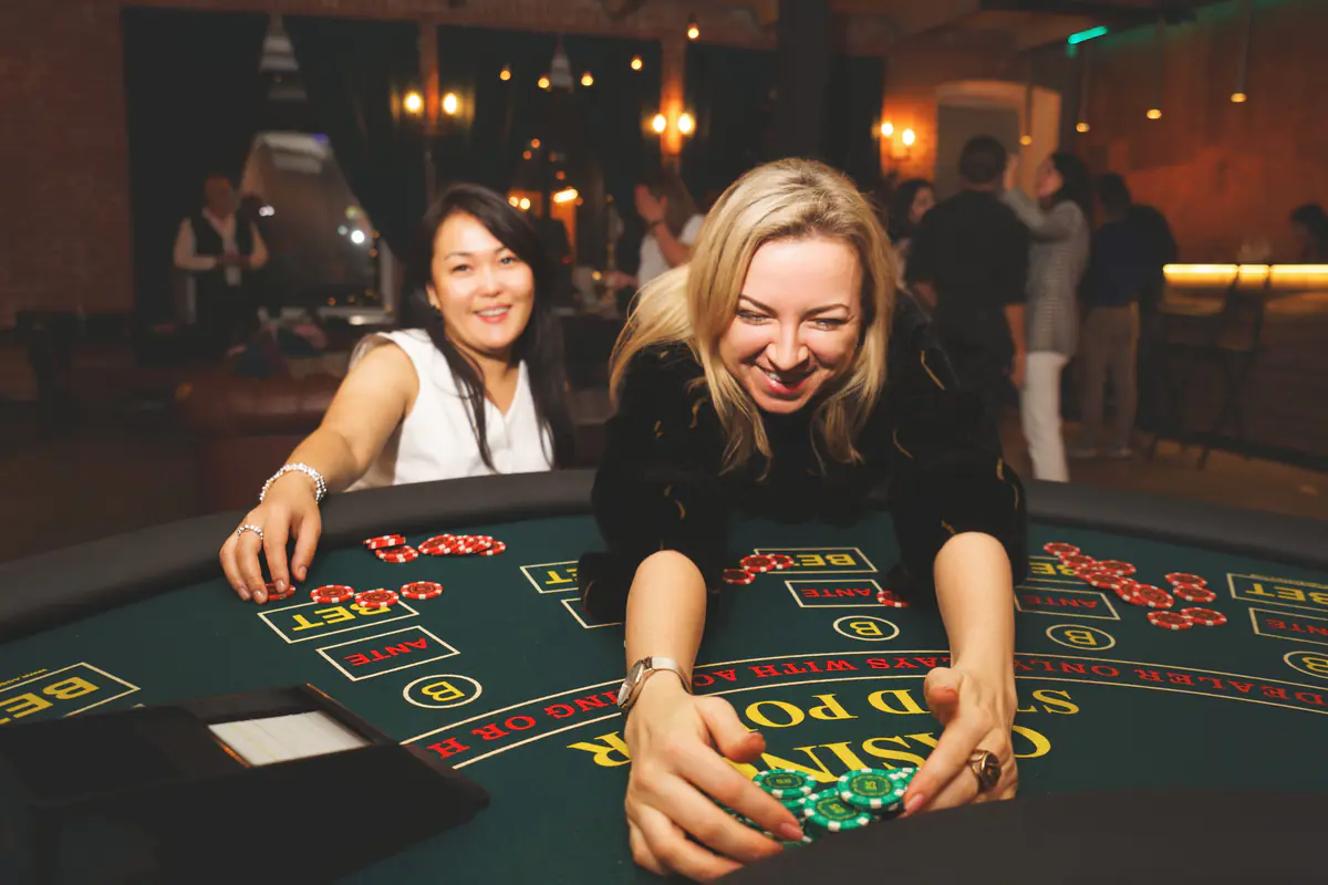 Девушка с улыбкой двумя руками двигает высокую стопку фишек по столу Casino Stud Poker