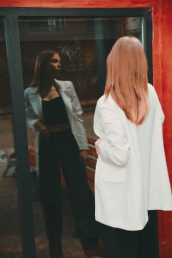 Фотография одинокой фигуры в белом пиджаке на фоне темного интерьера, передающая атмосферу задумчивости и одиночества.