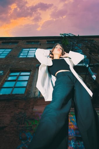 Фотография девушки на фоне обшарпанного фасада здания, передающая атмосферу заброшенности и уюта.